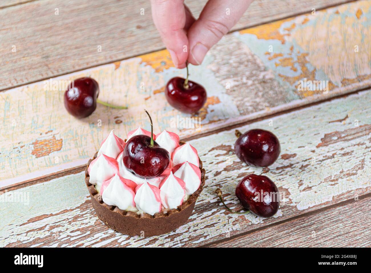 Schokoladen-Mini-Pie mit Schokoladenganache, gekrönt mit Schlagsahne und Kirsche. Im Hintergrund, Süßwaren Platzierung Kirschen. Stockfoto