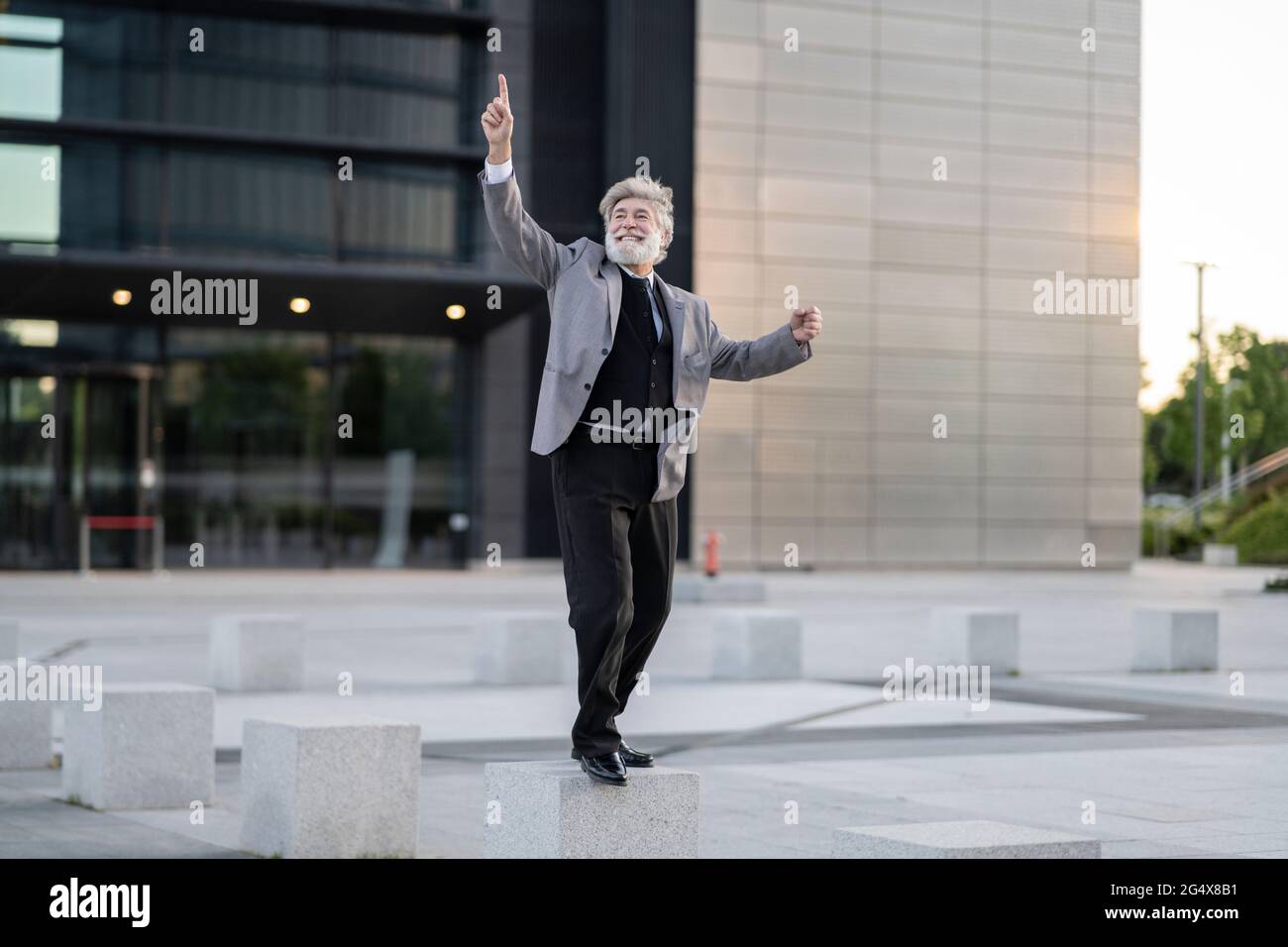 Fröhlicher Geschäftsmann, der auf Betonblöcken neben dem Bürogebäude tanzt Stockfoto