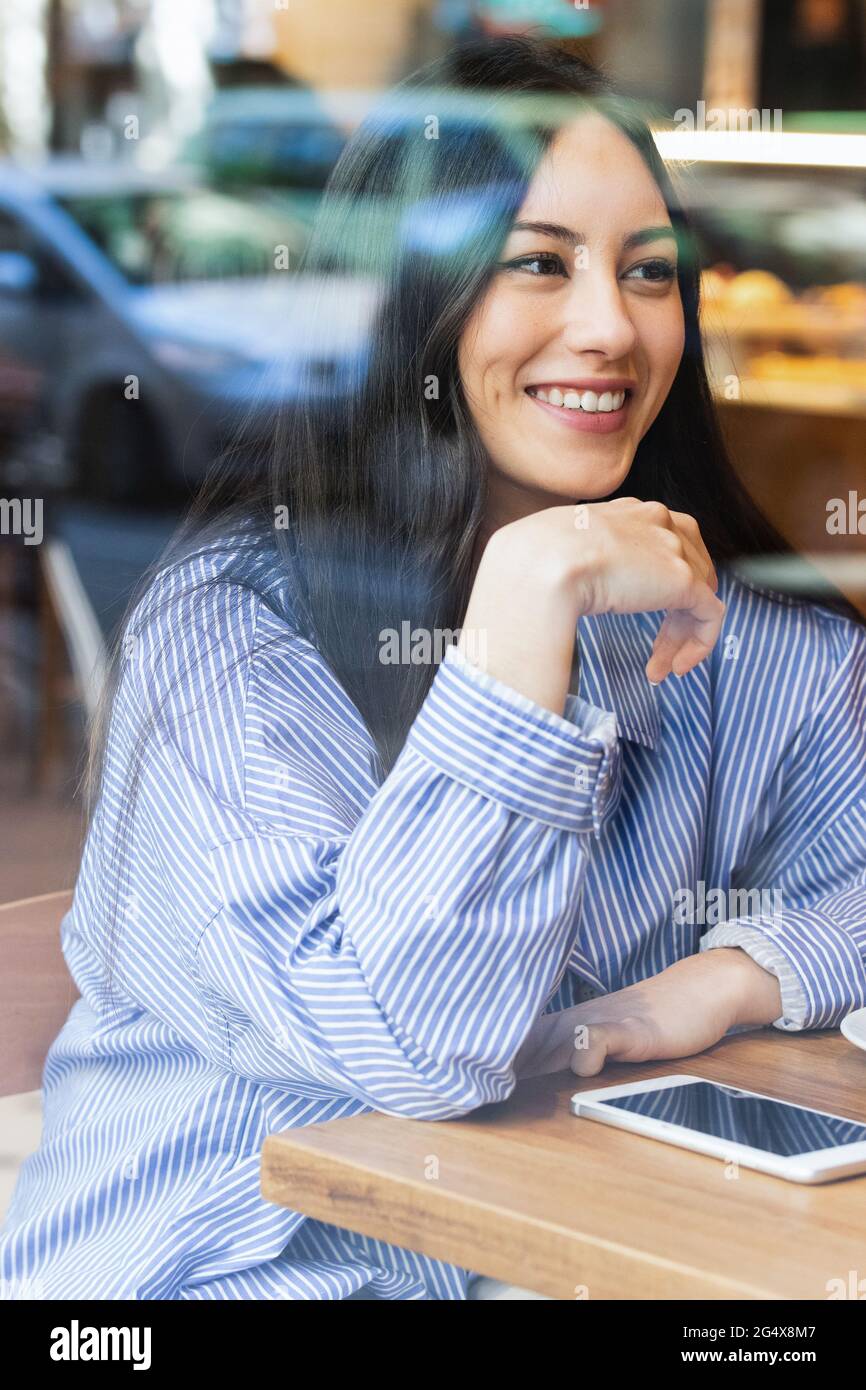 Schöne junge Frau, die in der Bar sitzt und durch das Glas gesehen wird Stockfoto