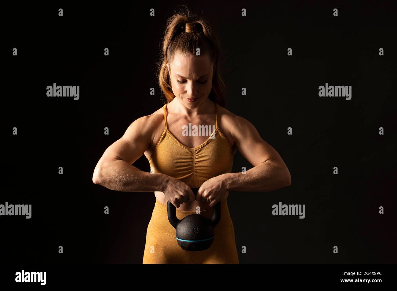 Lächelnde Sportlerin mit aktivem Ohr, die vor schwarzem Hintergrund steht Stockfoto