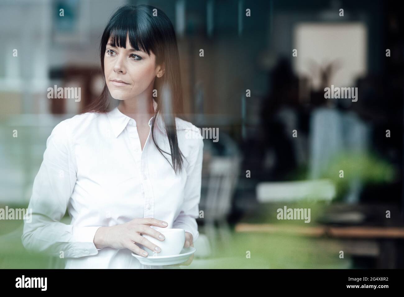 Reife weibliche Besitzerin mit Kaffeetasse, die auf das Café schaut Stockfoto