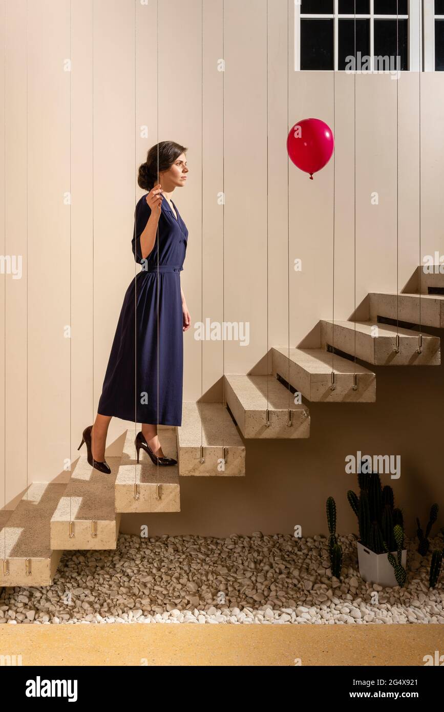 Frau, die auf den roten Heliumballon schaut, während sie sich auf der Treppe nach oben bewegt Stockfoto