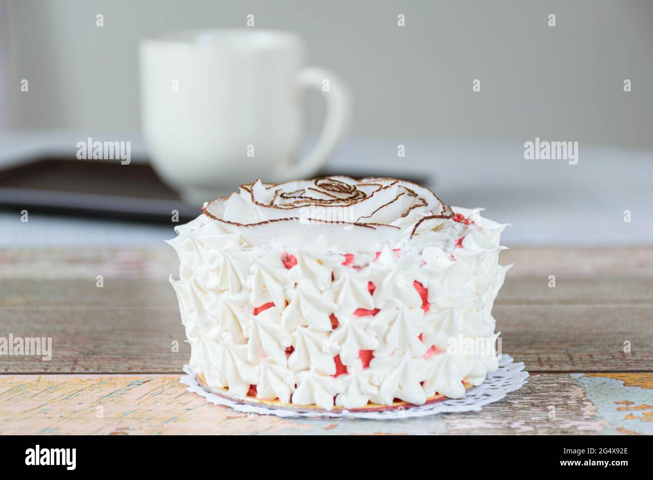 Mini-Vanillekuchen mit getrockneten Kokosnusschips und Schlagsahne dekoriert. Im Hintergrund eine verschwommene Tasse Kaffee. Stockfoto
