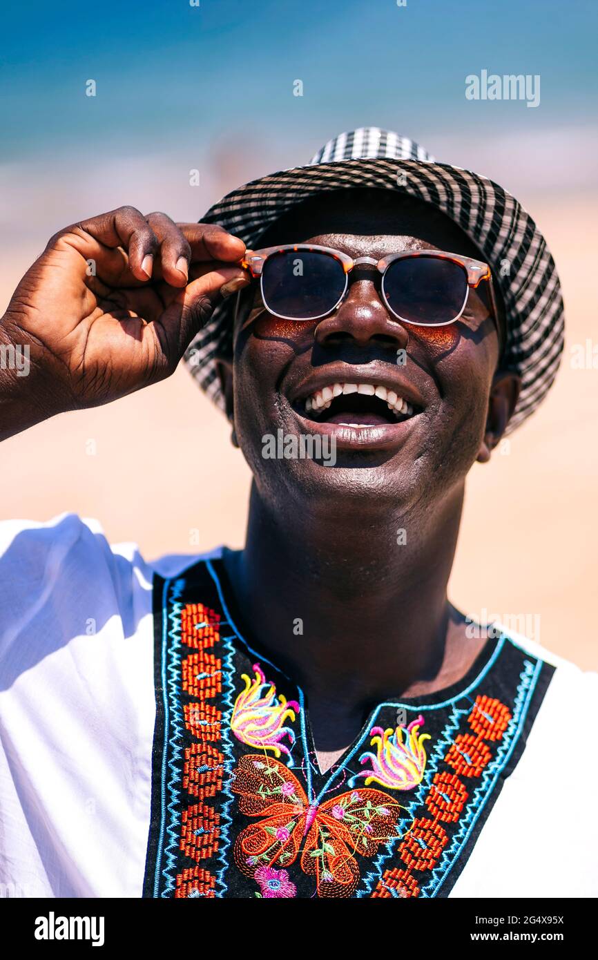 Fröhlicher Mann mit Hut, der an sonnigen Tagen eine Sonnenbrille anpasst Stockfoto