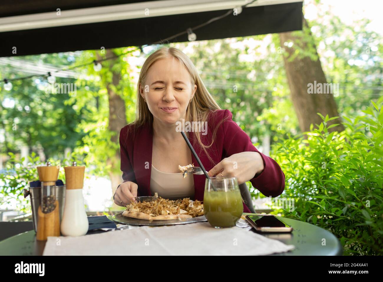 Junge blonde Frau mit geschlossenen Augen beim Essen im Café Stockfoto