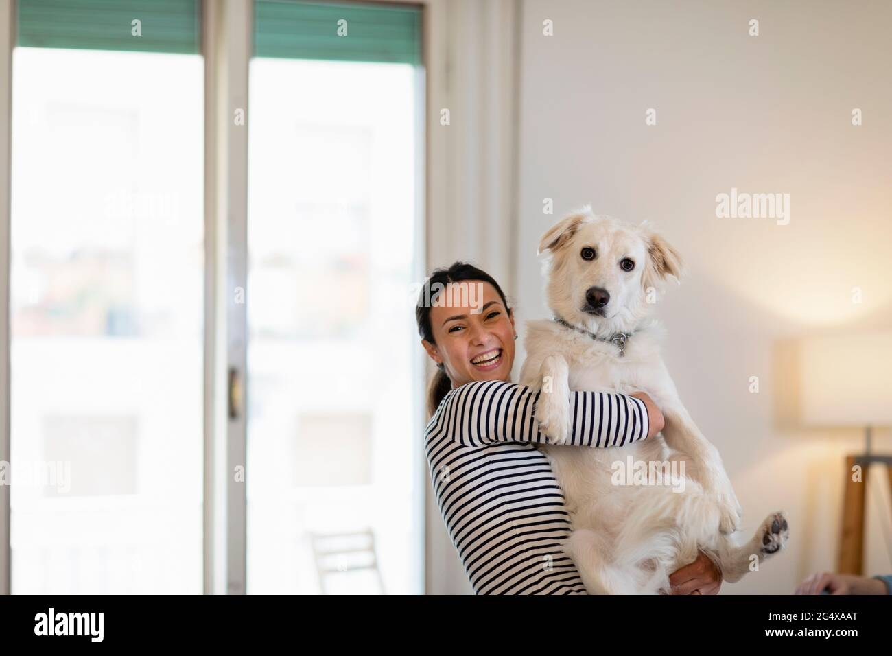 Fröhliche Besitzerin, die Hund zu Hause hält Stockfoto