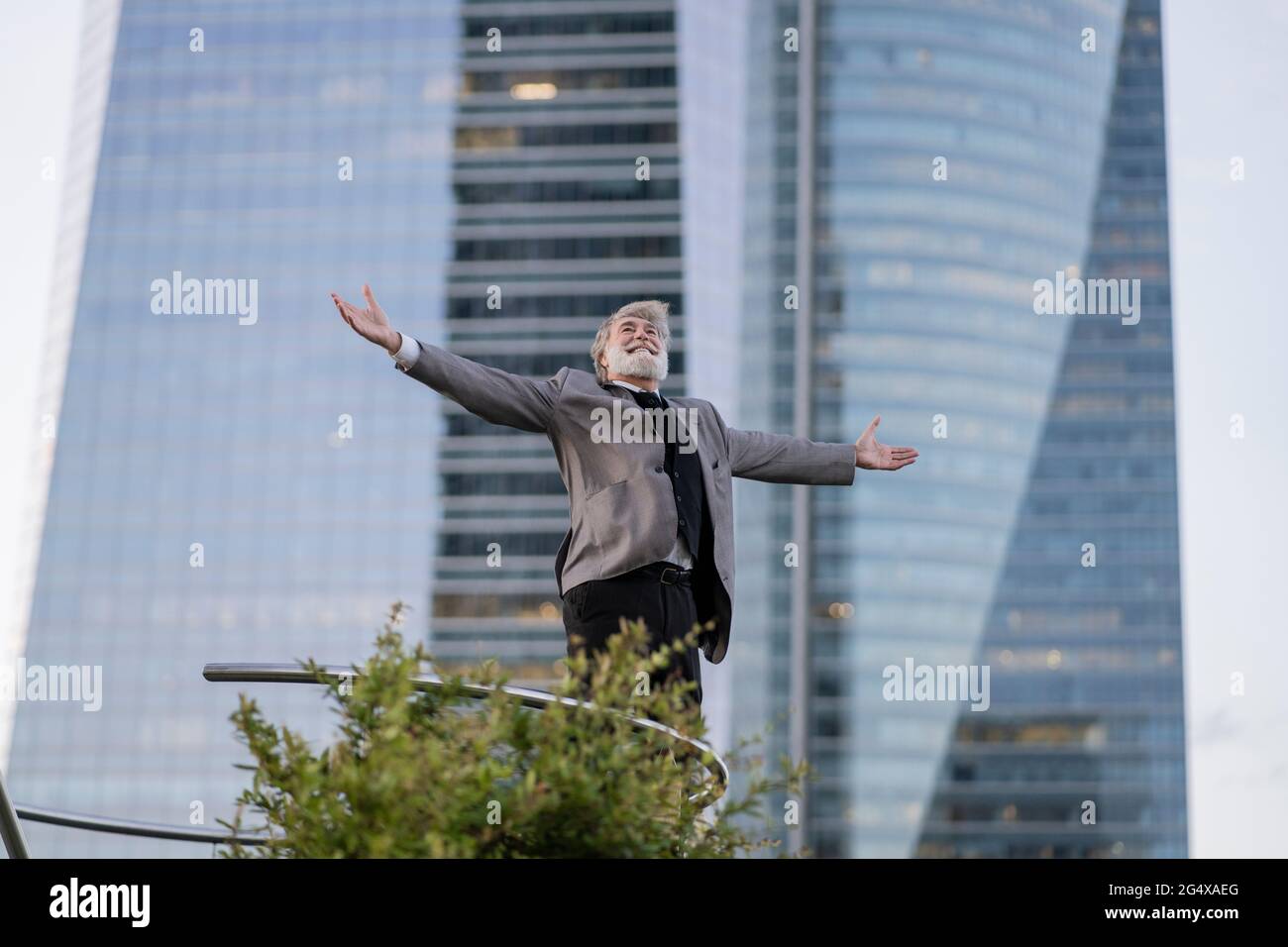 Ekstatischer Geschäftsmann, der mit ausgestreckten Armen vor dem Bürogebäude steht Stockfoto