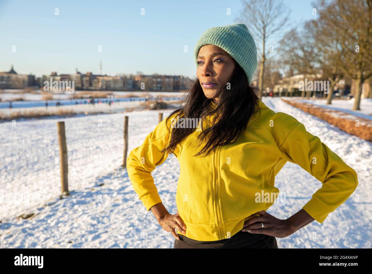 Reife Frau mit Strickmütze, die mit den Händen auf der Hüfte steht, während sie wegschaut Stockfoto