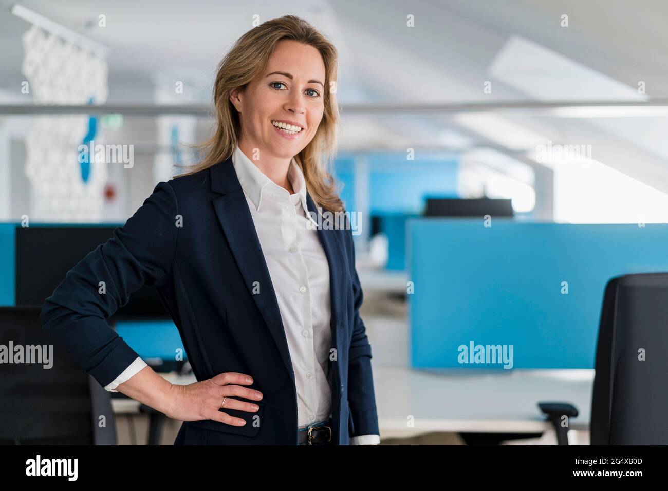 Lächelnde Unternehmerin mit Hand auf Hüfte im Büro Stockfoto