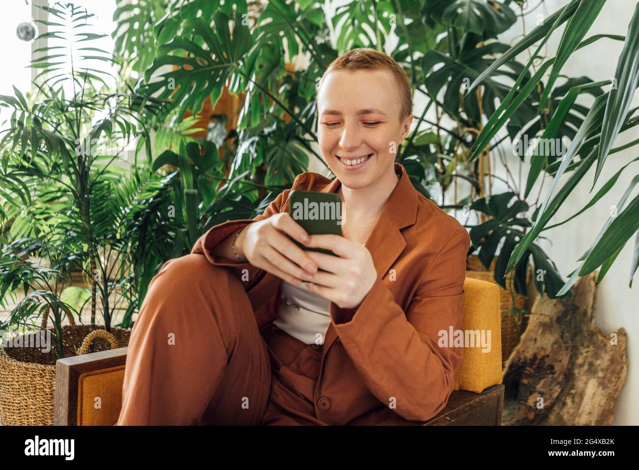 Lächelnde junge Geschäftsfrau mit Smartphone im grünen Büro Stockfoto