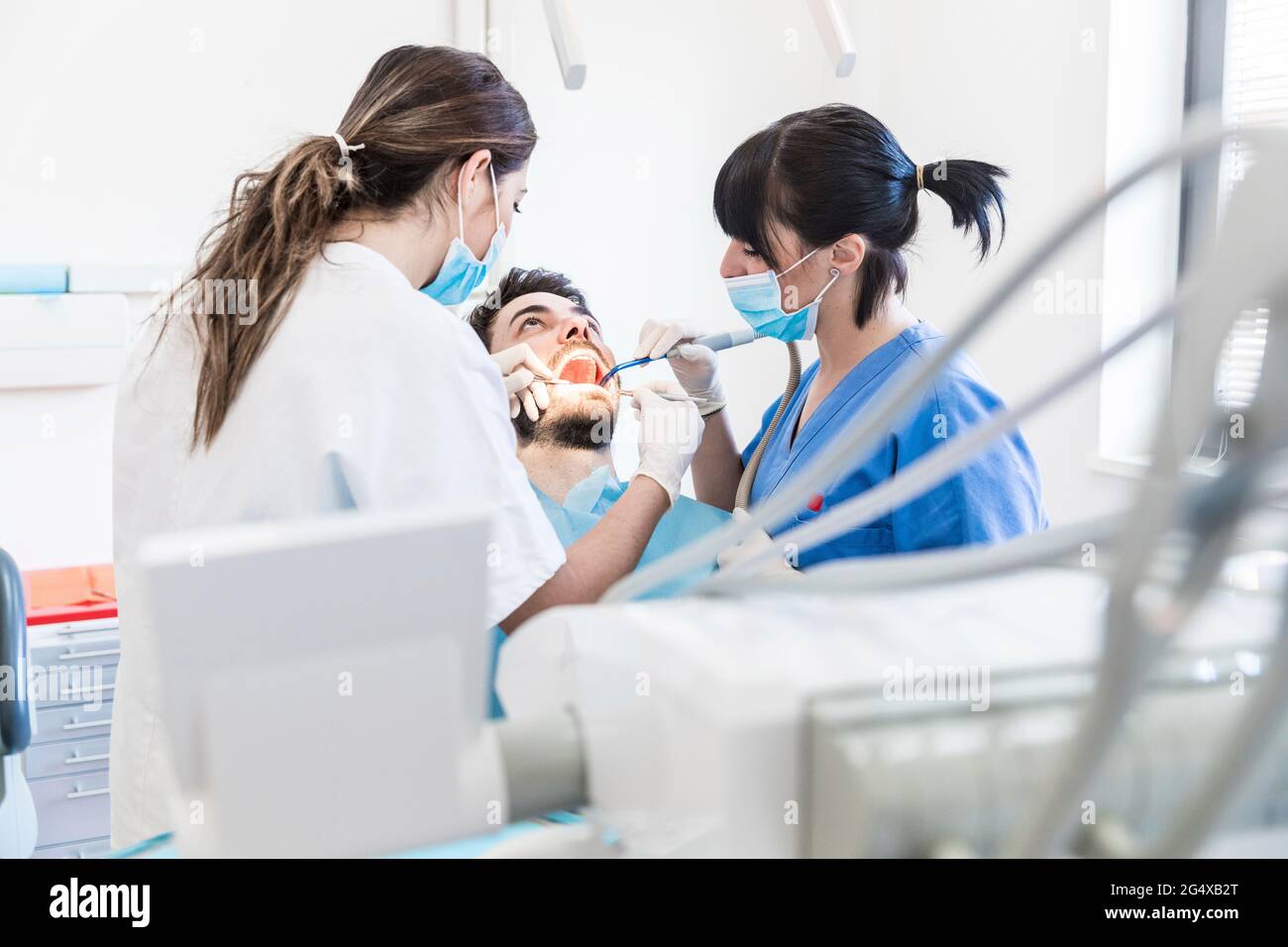 Zahnärztin mit Assistentin, die in der Klinik die Zähne eines männlichen Patienten bohrt Stockfoto