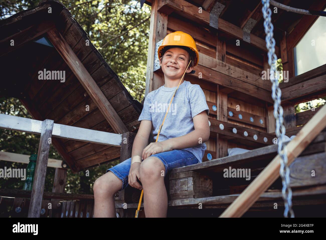 Nachdenklicher Junge in gelbem Hut, der in einem Holzhaus sitzt Stockfoto