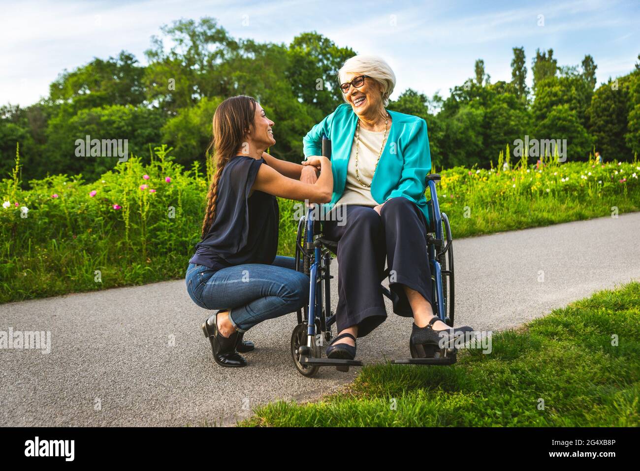 Lächelnde Enkelin im Gespräch mit Großmutter, die im Rollstuhl im Park sitzt Stockfoto
