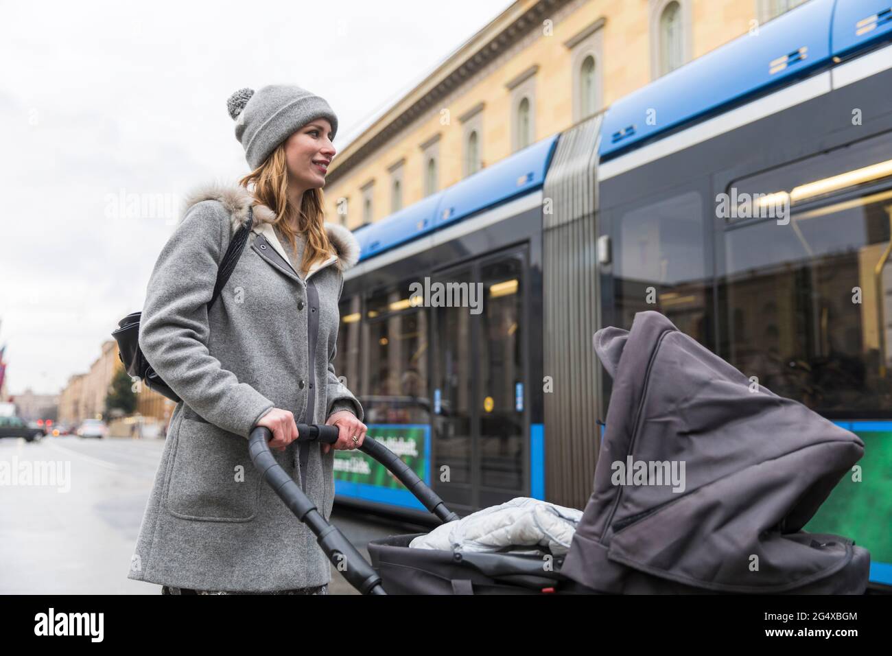 Lächelnde Frau, die den Kinderwagen schiebt, während sie in der Stadt spazieren geht Stockfoto