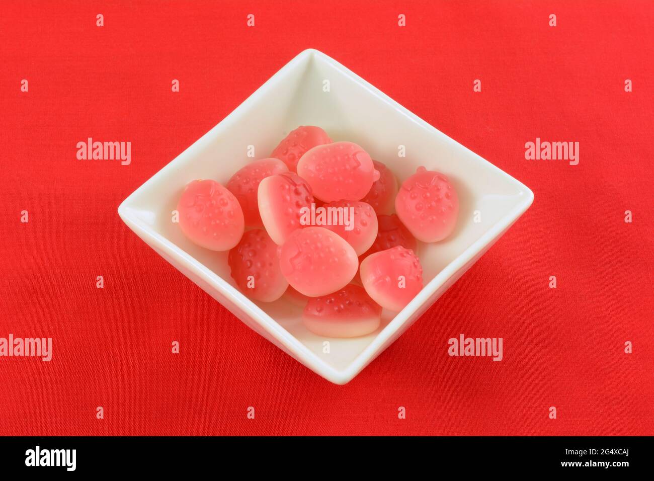 Erdbeerbonbon in Form von Erdbeerfrucht in weißer Süßigkeitenschale auf rotem Hintergrund Stockfoto