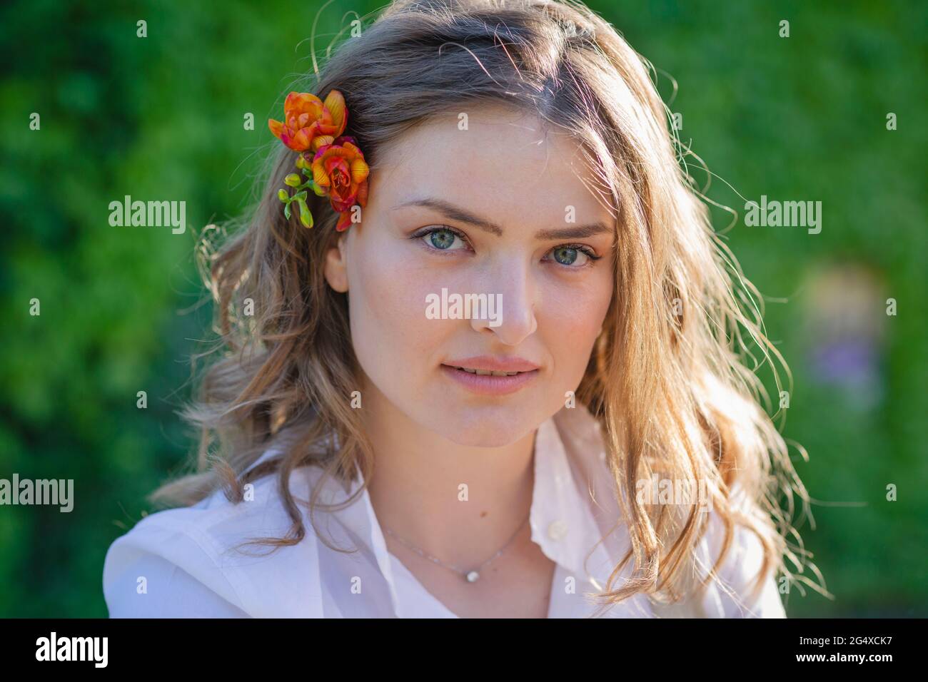 Schöne junge Frau mit braunem Haar trägt Freesia Blume an sonnigen Tagen Stockfoto