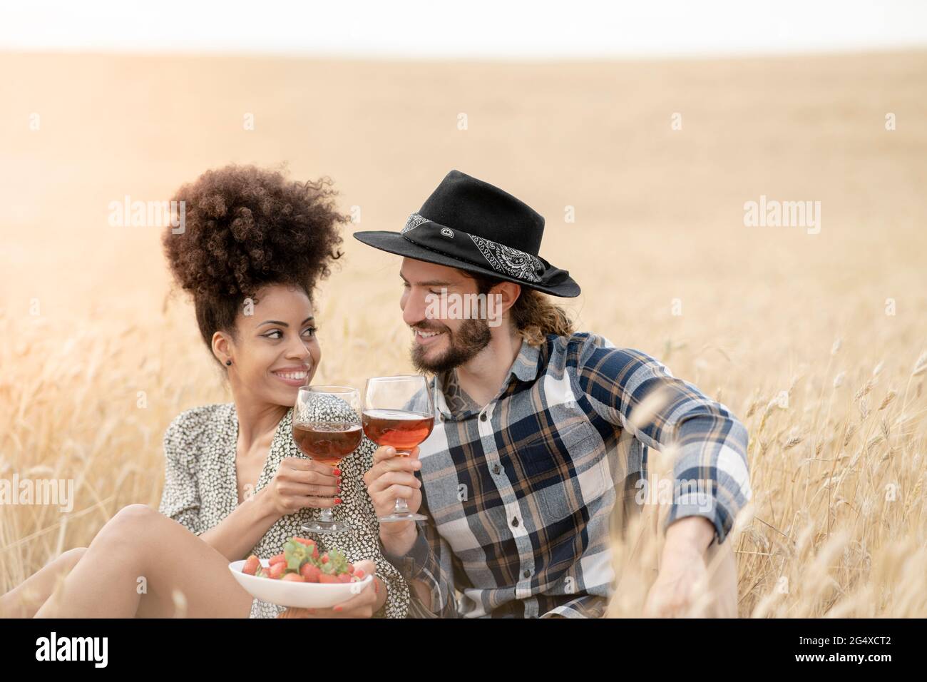 Während des Picknicks auf dem Feld sitzend ein paar toastende Getränke Stockfoto