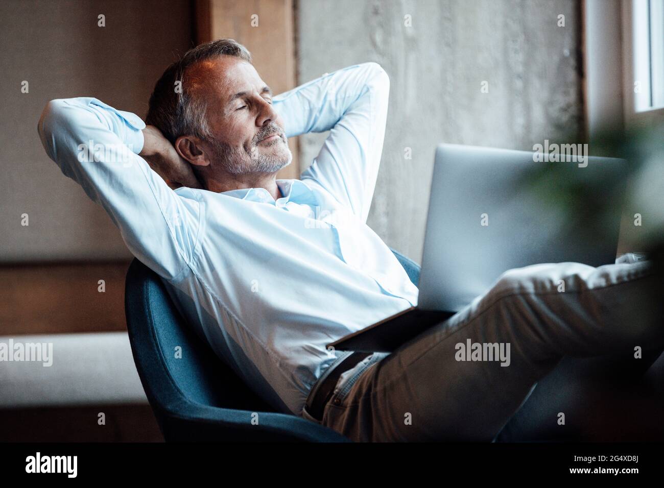 Älterer männlicher Unternehmer, der mit einem Laptop auf einem Stuhl sitzt Stockfoto