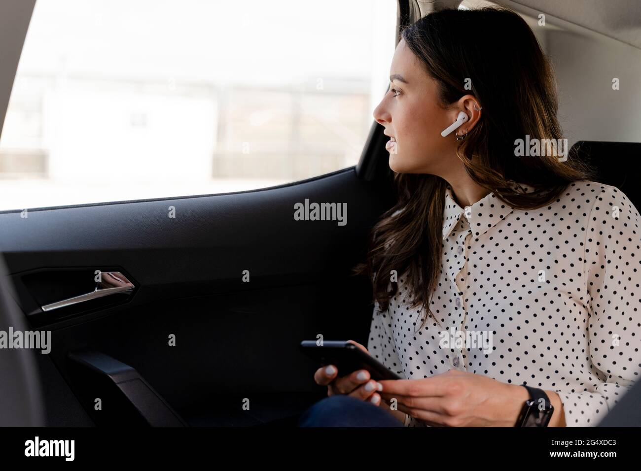 Eine professionelle Frau mit drahtlosen Technologien, die durch das Fenster schaut, während sie im Auto sitzt Stockfoto