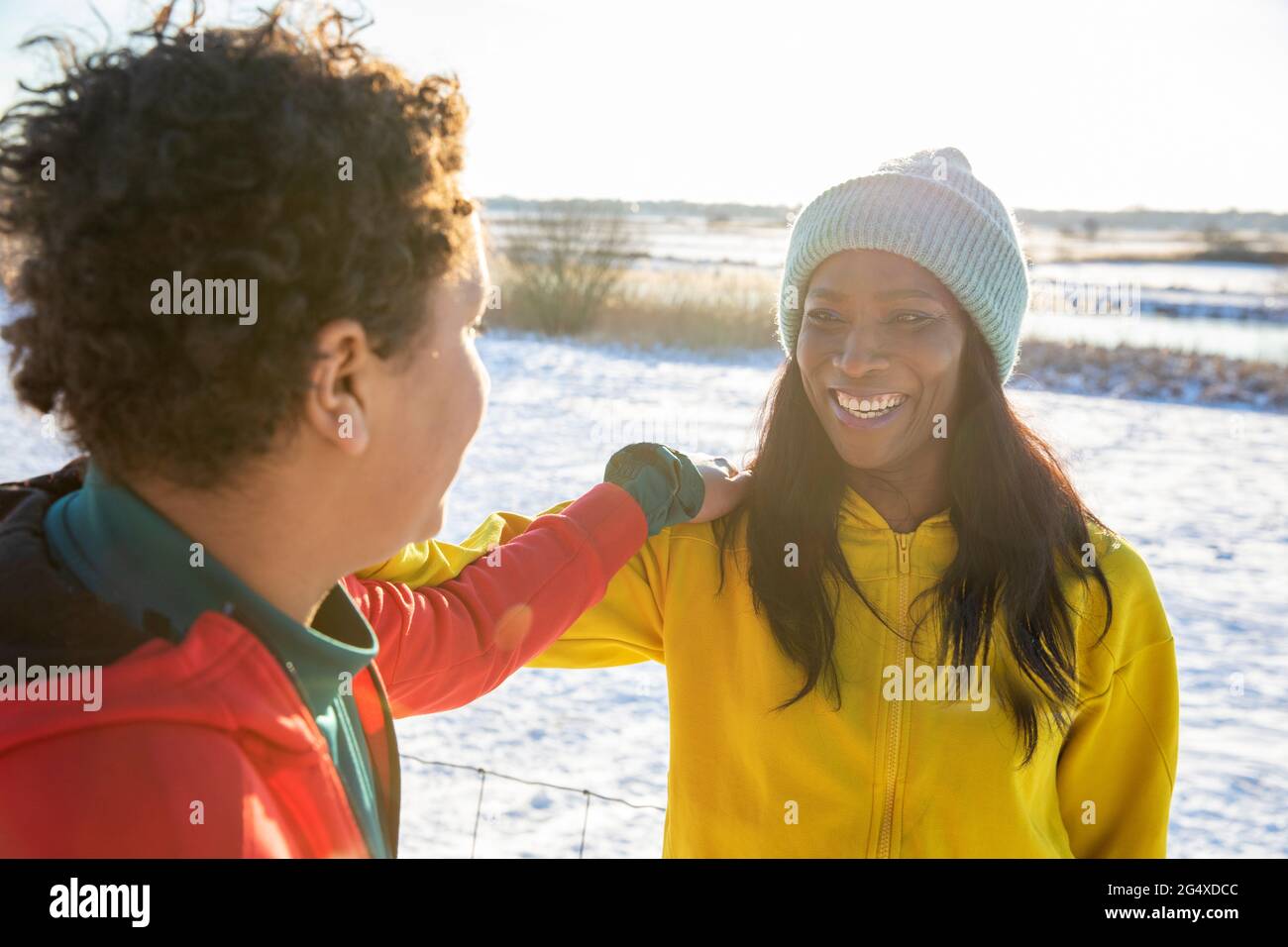 Fröhliche reife Frau, die im Winter mit der Hand auf der Schulter auf den Sohn schaut Stockfoto