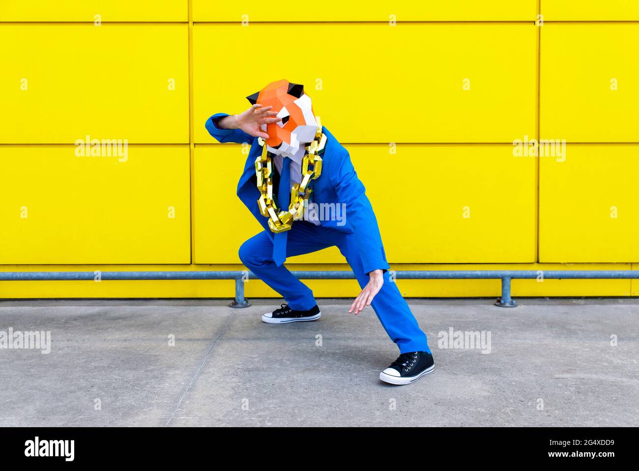 Mann mit leuchtend blauem Anzug und Tiger-Maske, der in Kampfhaltung vor der gelben Wand steht Stockfoto