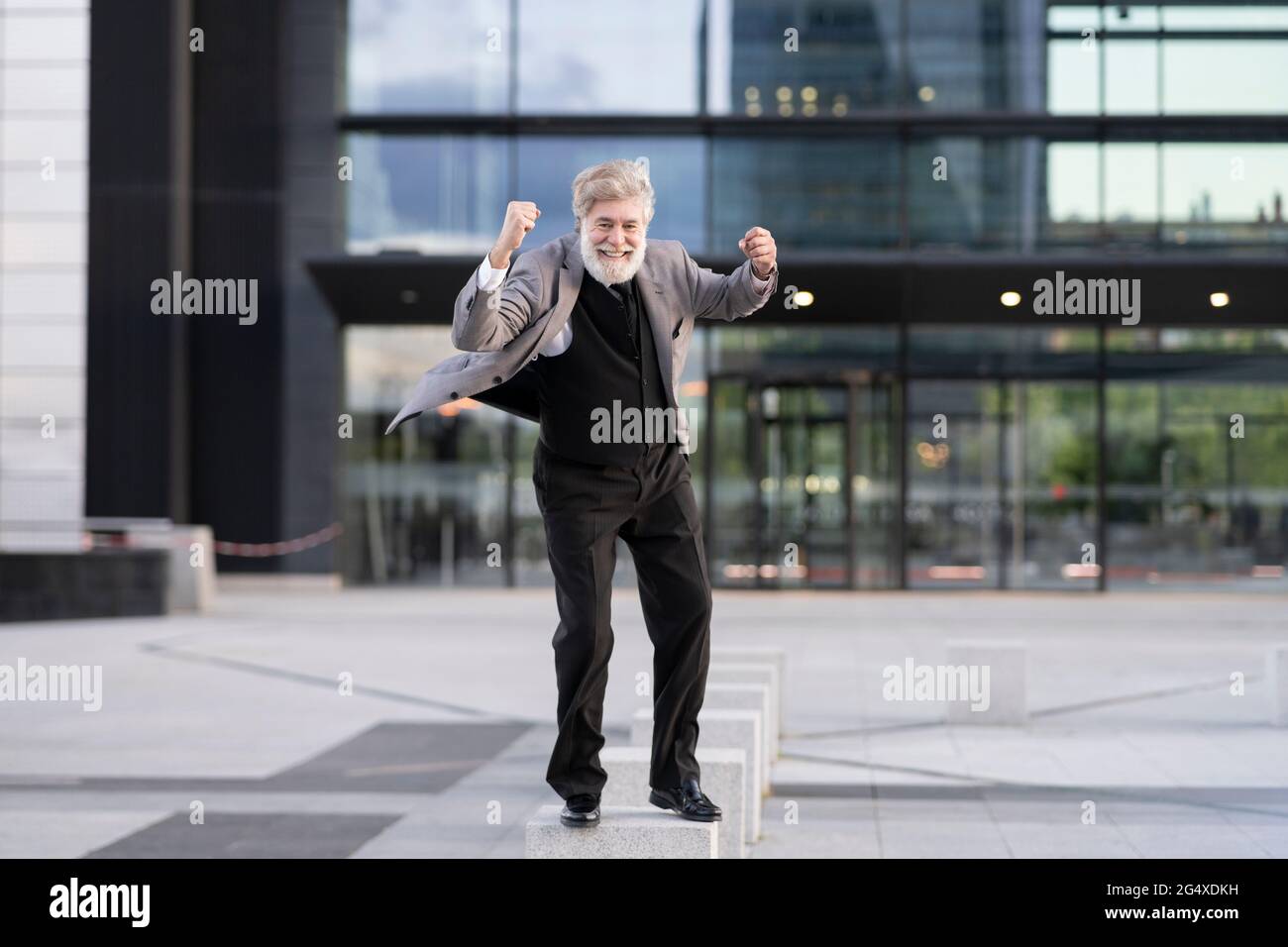 Ekstatischer Geschäftsmann, der auf einem Betonblock vor dem Bürogebäude steht Stockfoto