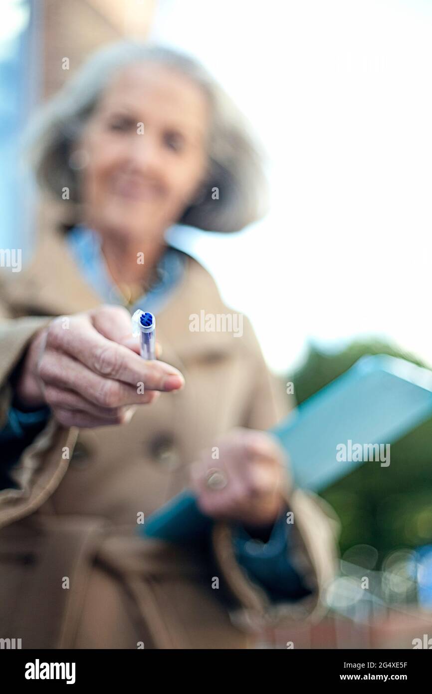 Ältere Frau mit Klemmbrett bietet Stift Stockfoto
