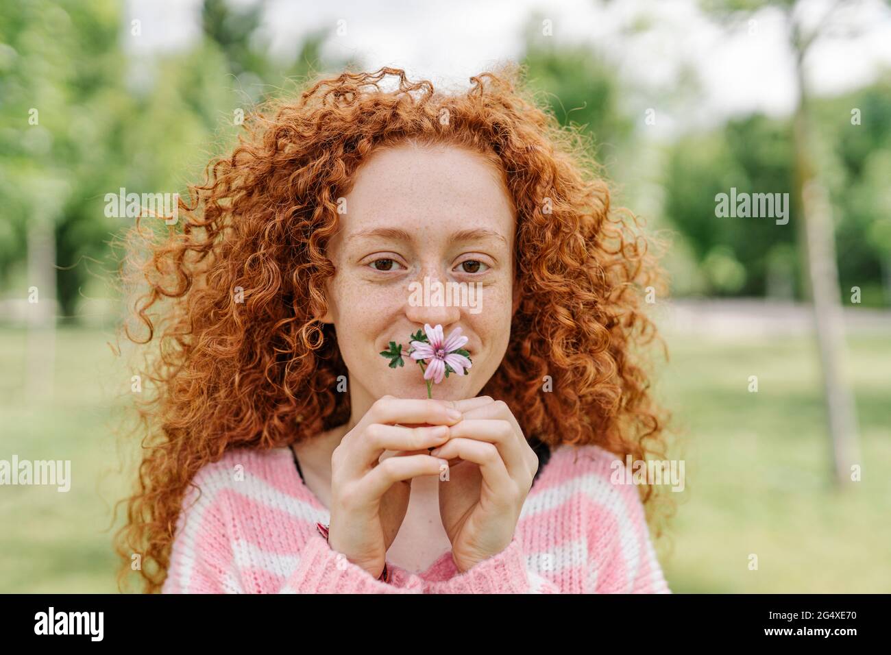 Rothaarige Frau mit lockigen Haaren bedeckt den Mund mit Blume Stockfoto