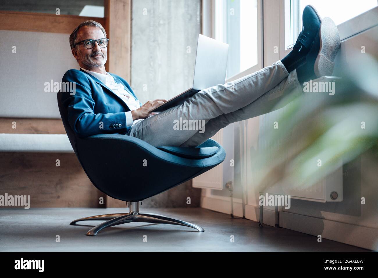 Älterer männlicher Unternehmer, der im Büro mit einem Laptop auf dem Schoß sitzt Stockfoto