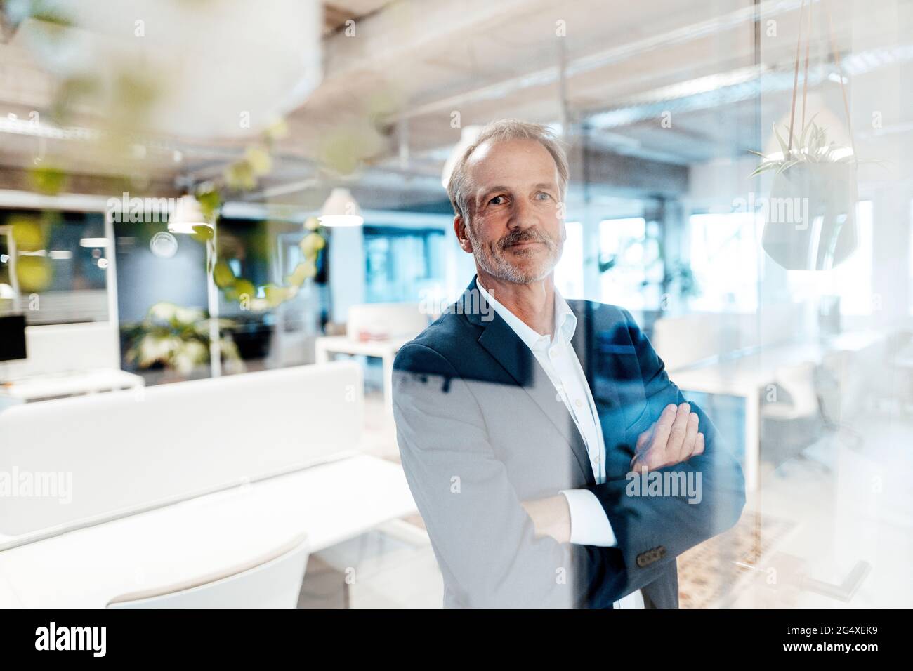 Leitender männlicher Unternehmer mit von einer Glaswand durchzogenen Armen im Büro Stockfoto