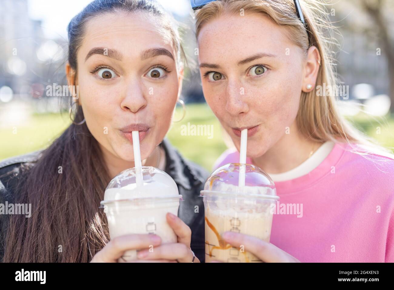 Überraschte Freundinnen, die Milchshakes im Park tranken Stockfoto