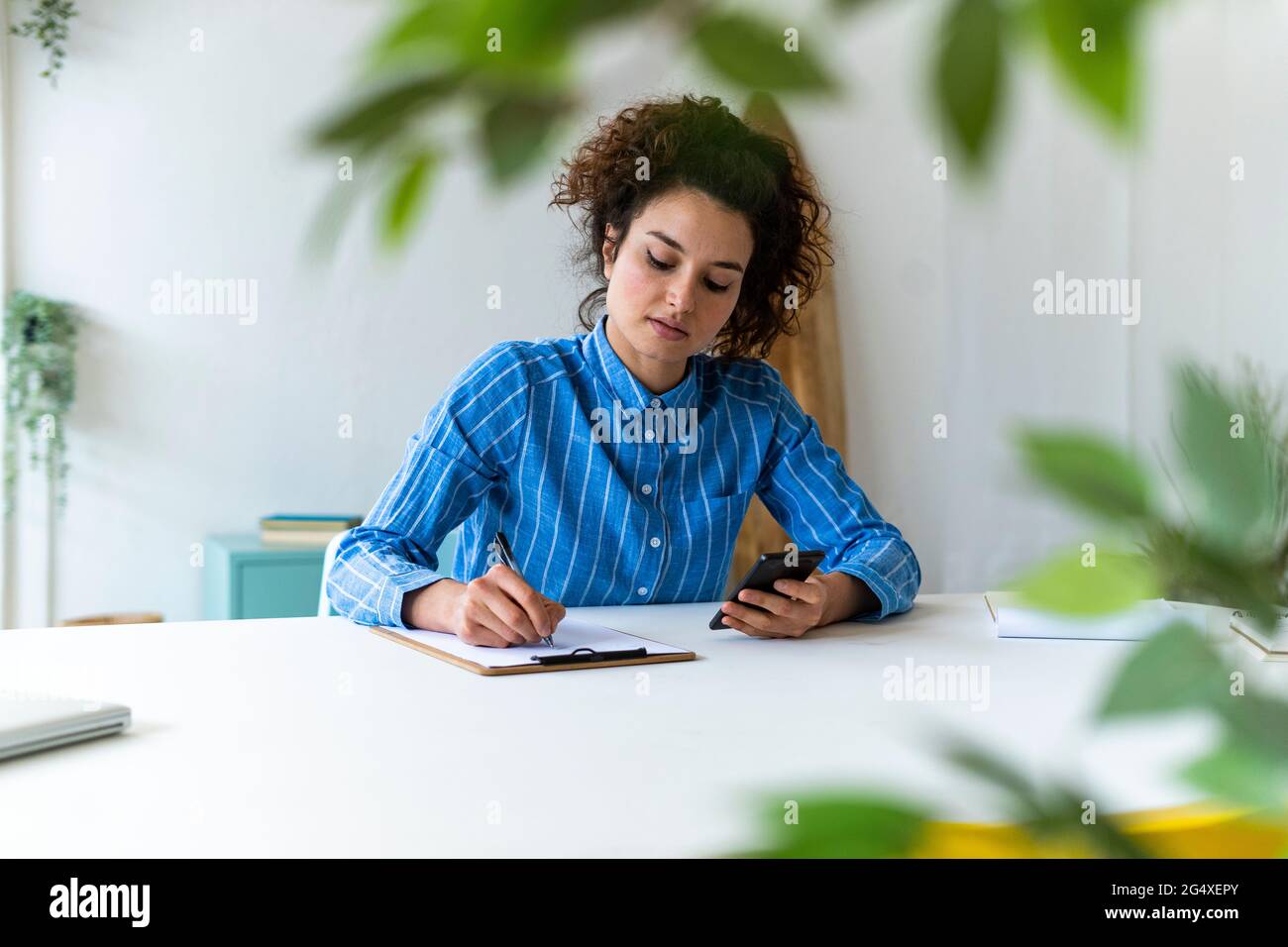 Geschäftsfrau mit Mobiltelefon, die am kreativen Arbeitsplatz arbeitet Stockfoto