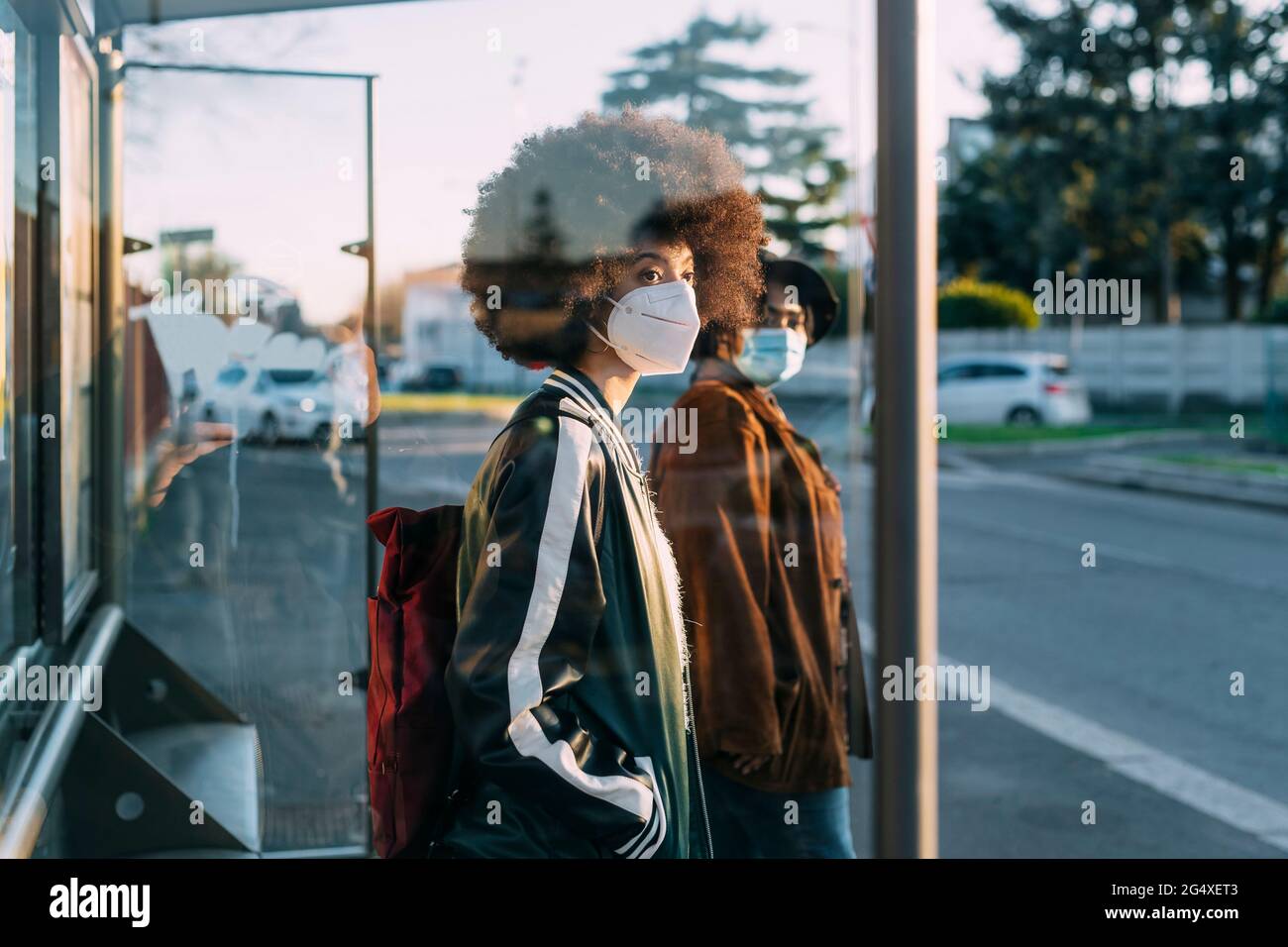 Freunde mit Gesichtsmaske warten während des Sonnenuntergangs am Busbahnhof Stockfoto