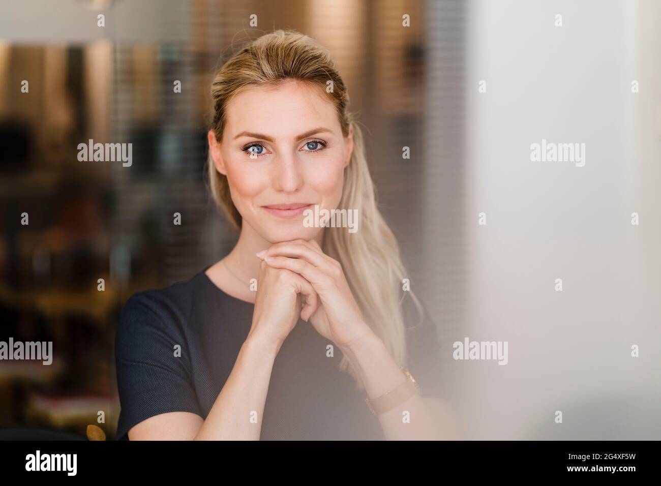Schöne lächelnde Unternehmerin, die im Büro mit der Hand auf dem Kinn sitzt Stockfoto