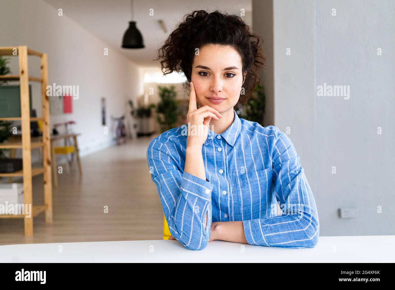 Weibliche Unternehmerin mit der Hand am Kinn, die im Büro am Schreibtisch sitzt Stockfoto