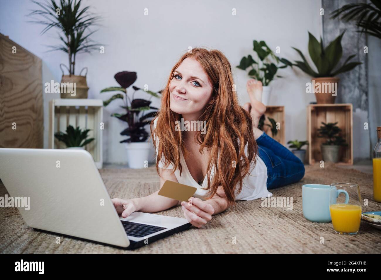 Lächelnde Rothaarige Frau mit Kreditkarte beim Online-Shopping auf dem Laptop zu Hause Stockfoto