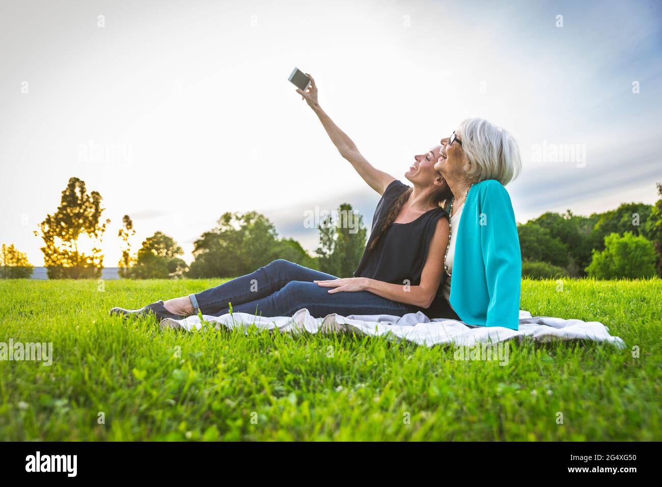 Lächelnde Frauen, die Selfie über das Mobiltelefon machen, während sie auf der Wiese sitzen Stockfoto