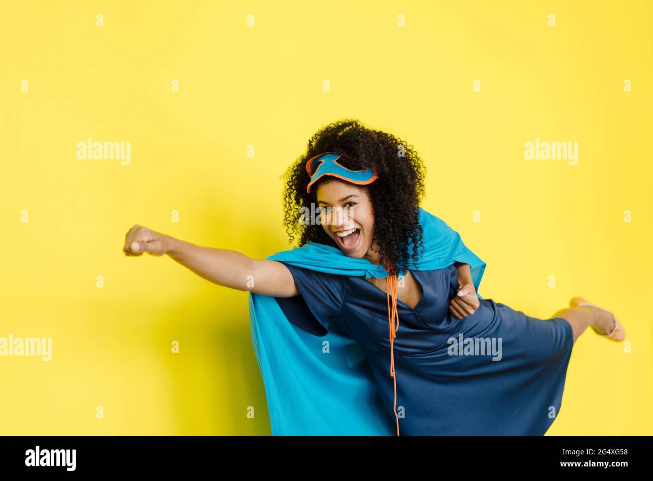 Fröhliche Frau trägt ein Superhelden-Kostüm, das auf gelbem Hintergrund fliegt Stockfoto