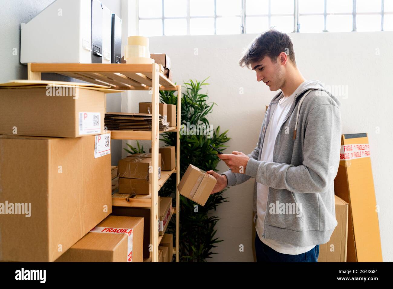 Männlicher Unternehmer, der QR-Code durch ein Smartphone vor dem Regal im Lager scannt Stockfoto