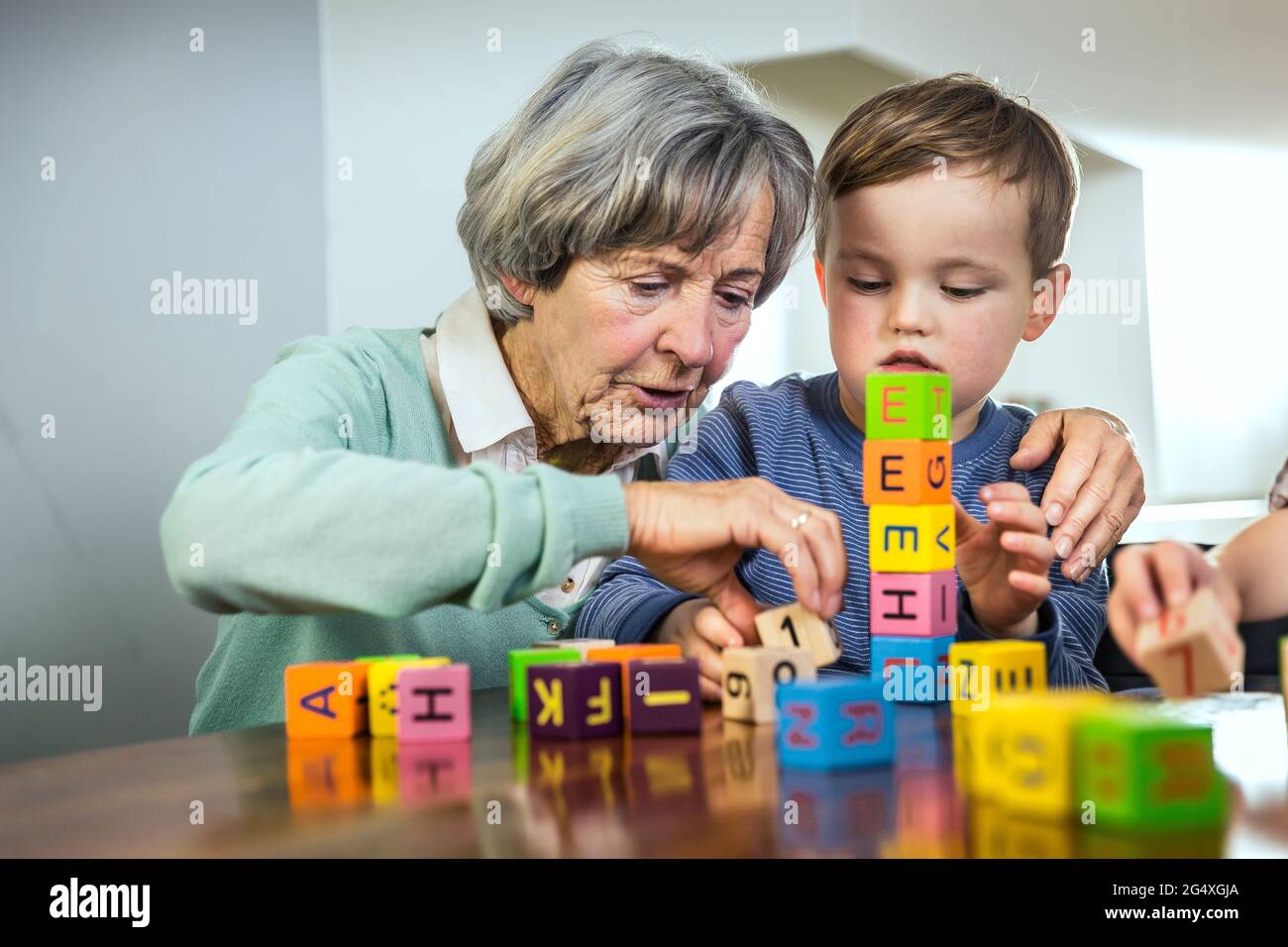 Großmutter hilft Enkel stapeln Spielzeugblöcke zu Hause Stockfoto