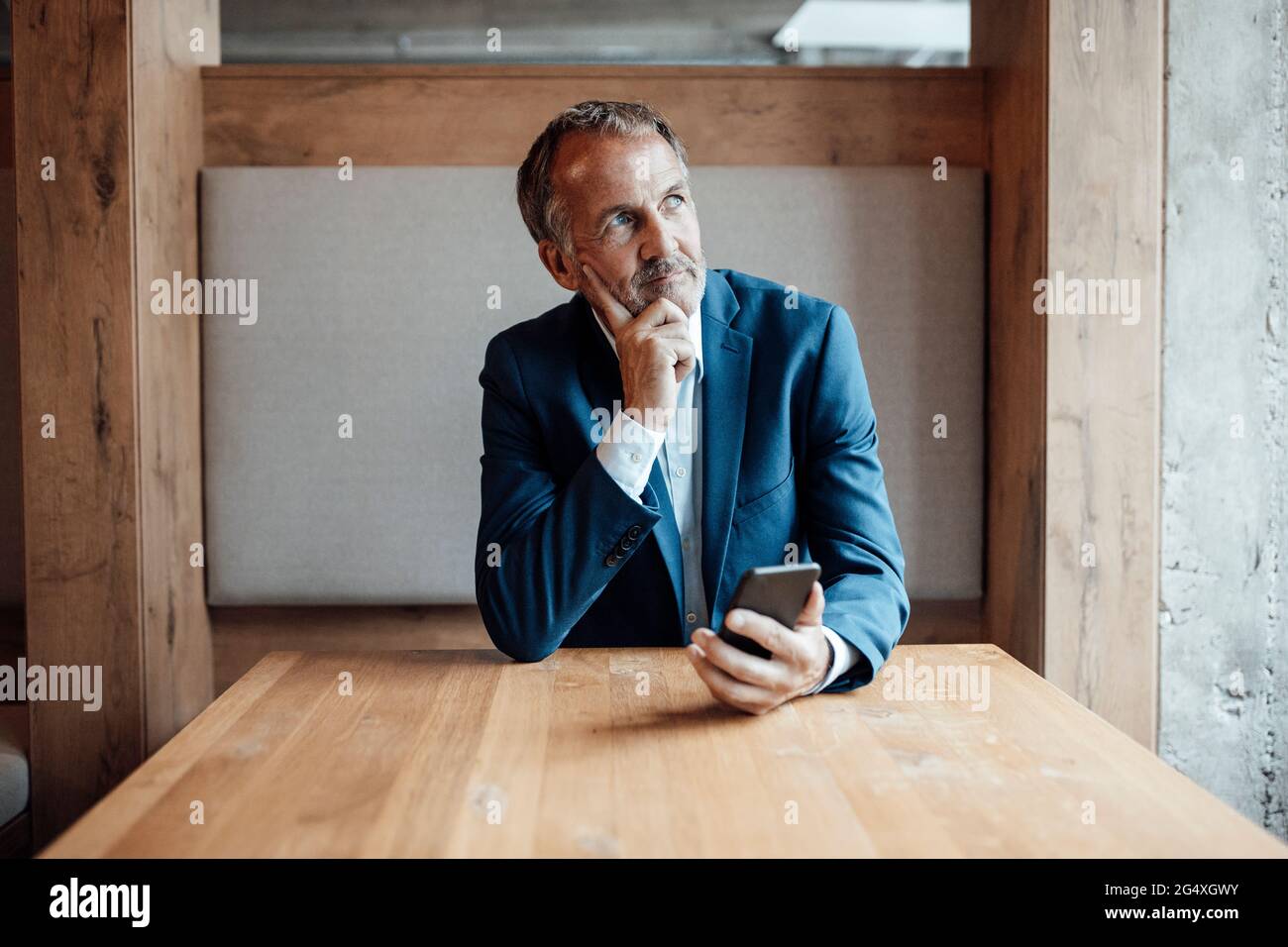 Leitender männlicher Unternehmer mit der Hand am Kinn, der im Büro am Tisch sitzt Stockfoto