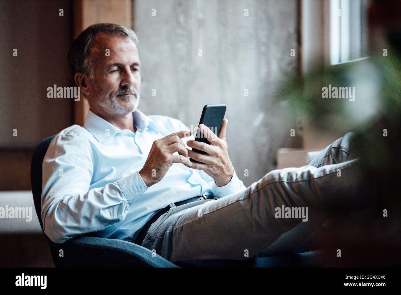 Leitender männlicher Unternehmer, der im Büro mit dem Mobiltelefon sitzt Stockfoto