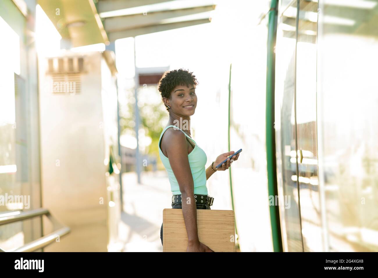 Junge junge Frau, die mit drahtlosen Technologien am Straßenbahneingang steht Stockfoto