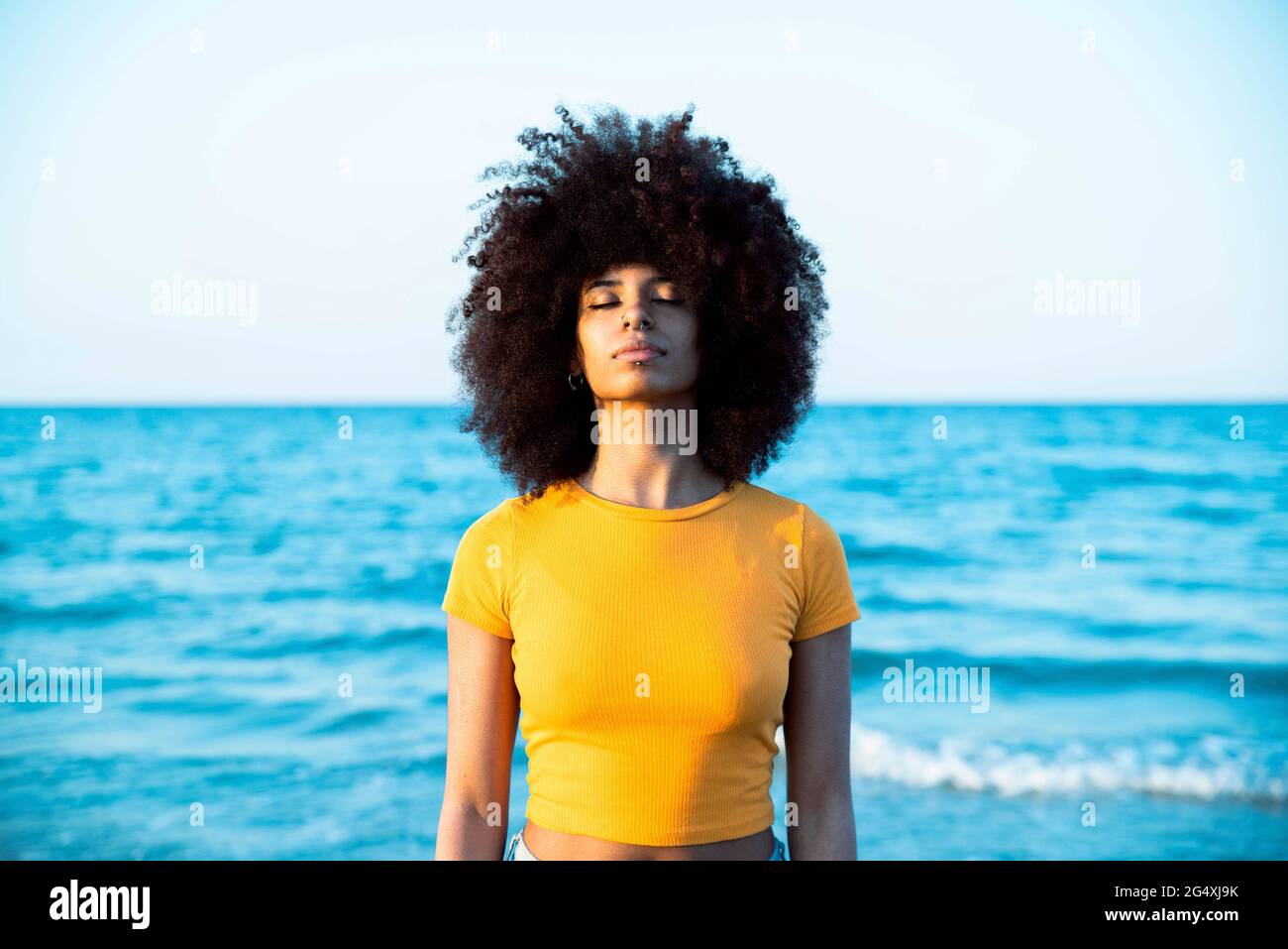 Junge Afro-Frau mit geschlossenen Augen am Strand stehend Stockfoto