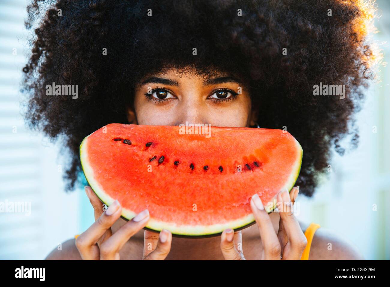 Afro-Frau bedeckt das Gesicht mit einer Scheibe Wassermelone Stockfoto