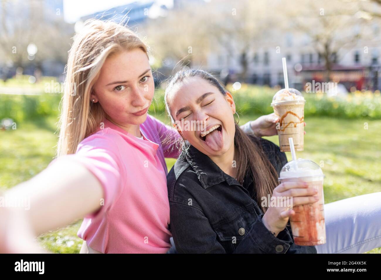 Junge Frau, die ein Gesicht von einer Freundin beim Milchshake im Park macht Stockfoto