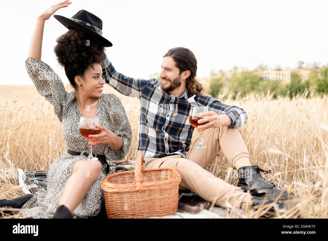 Ein Paar mit mittlerem Erwachsenen und einem Getränk, während man auf dem Feld sitzt Stockfoto