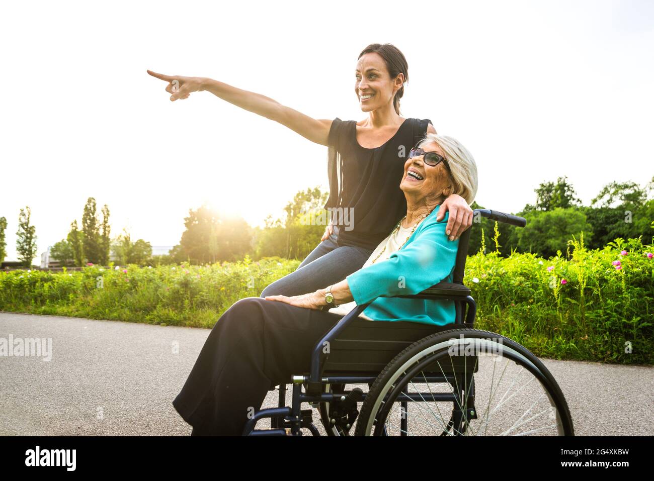 Lächelnde Enkelin zeigt mit Großmutter, die im Rollstuhl auf den Park sitzt Stockfoto