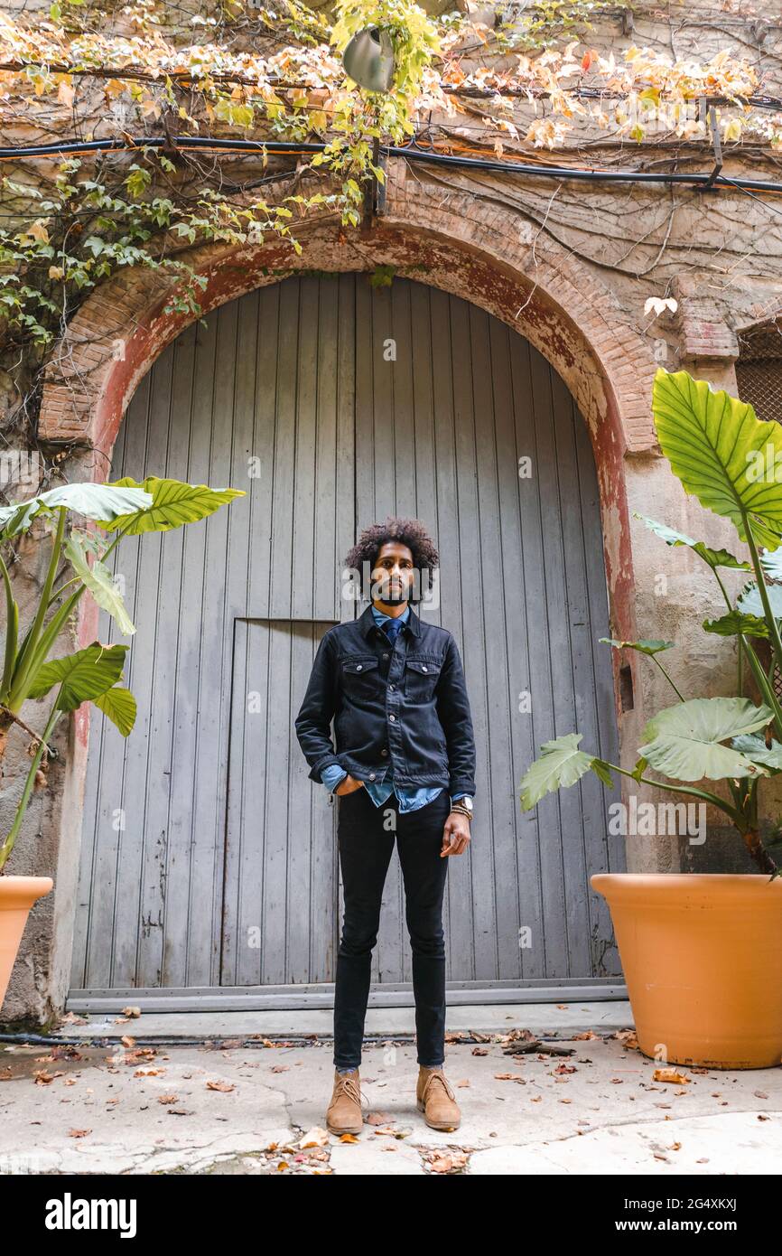 Junger modischer Mann mit der Hand in der Tasche, der vor dem Tor steht Stockfoto