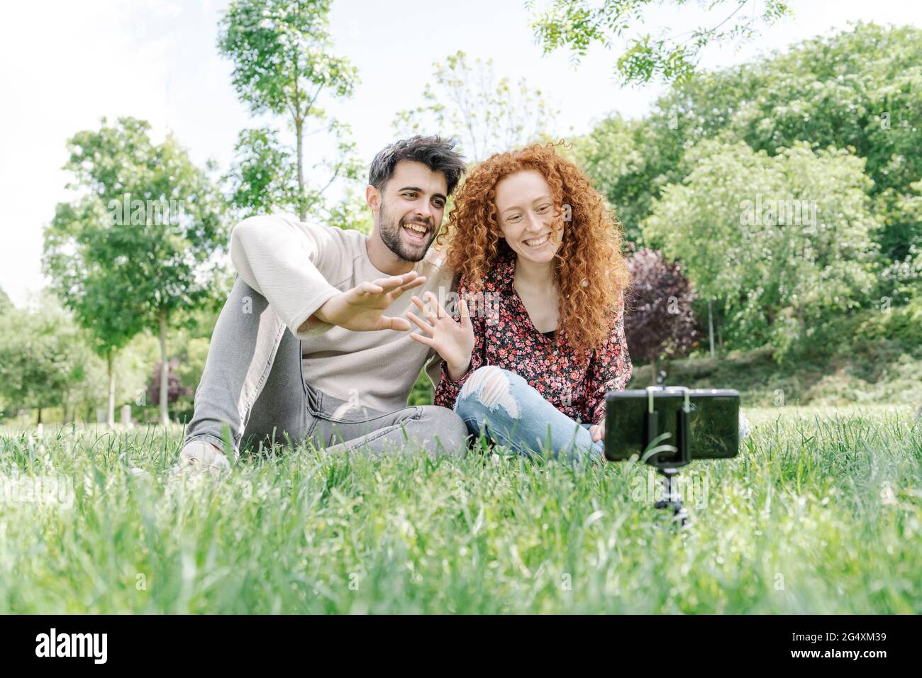 Glückliches junges Paar winkt beim Vlogging im öffentlichen Park Stockfoto